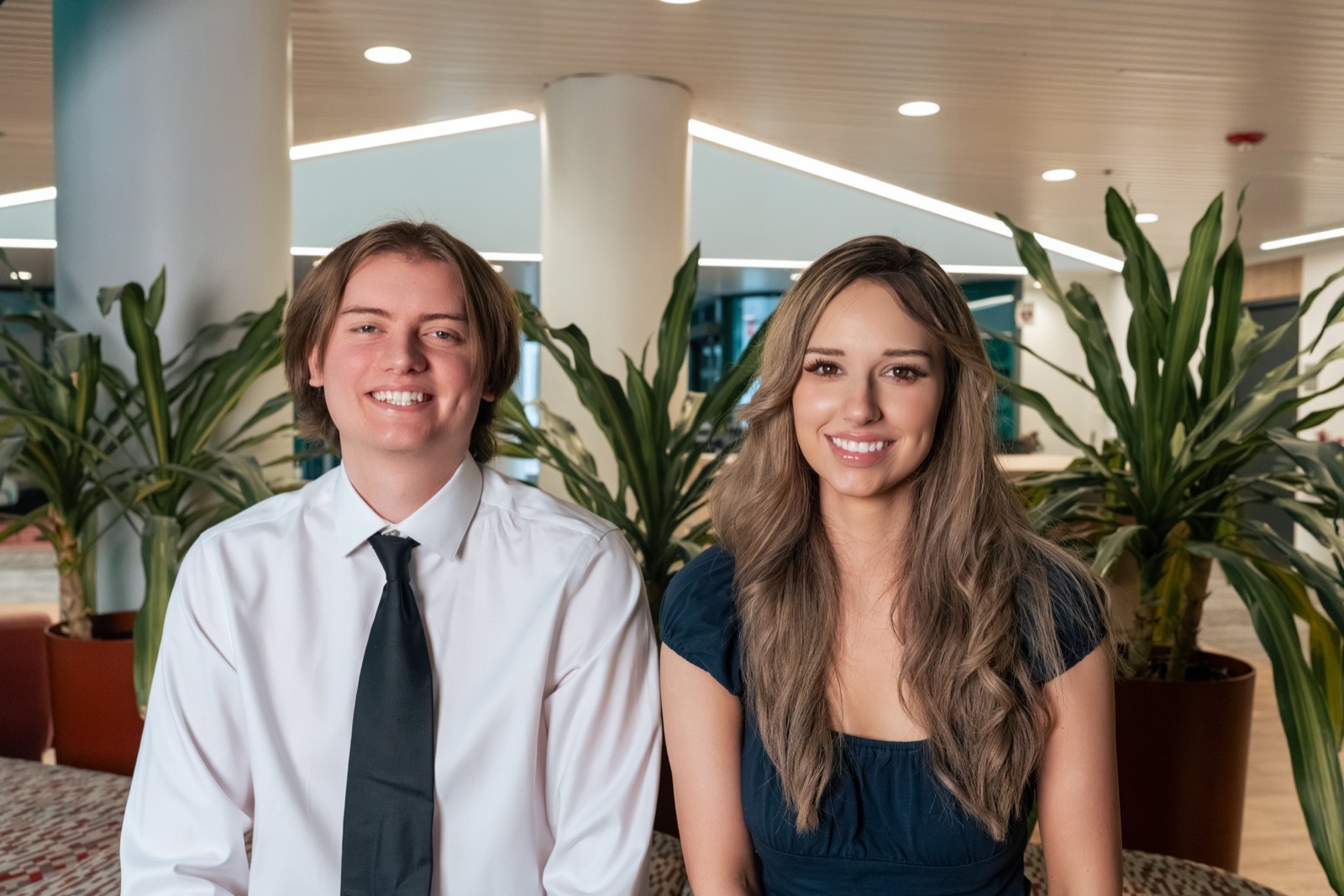 Grace Clark, Co-Founder, and Joe Tracy, Co-Founder of Snapfire Automations, smiling together indoors in an office lobby with green plants in the background.